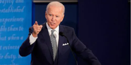 A man in a dark suit pointing as he speaks at a lectern